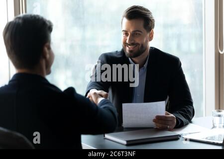 Smiling young handsome businessman shaking hands with male confident partner. Stock Photo