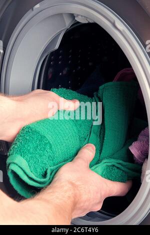 Man taking color clothes from washing machine. A drum of washing machine full of dirty laundry in bathroom. Stock Photo