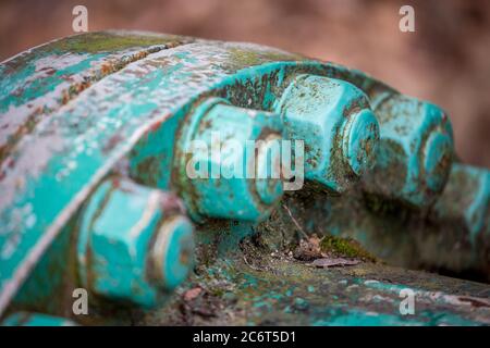 Selective extremely shallow focus close up of big nuts and bolts covered in layers of rust and old paint. Partial colorful view of round water supply pipe connection section. Natural daytime light Stock Photo