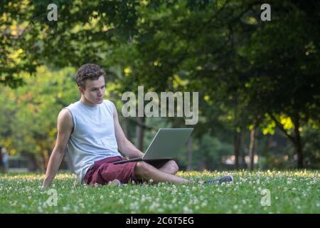 Young man in the park sitting on the grass with a laptop. Stock Photo