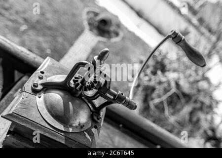 Vintage manual coffee grinder or mill, monochromatic metal high-contrast black and white picture. Partial diagonal composition view from above. Shallow selective focus on transmission elements Stock Photo