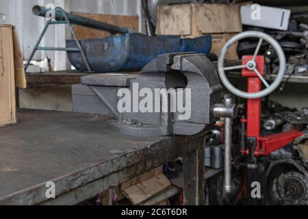 Old metal Bench Vise on steel table at workshop. Metal clamps. Stock Photo