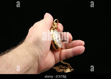 Black background of old man's hand holding gold pocket watch with chain. Stock Photo