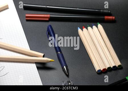 White notebook , color pencils, felt pen and pencil sharpener on a table against black background. Preparing for a school. Back to school. Stock Photo
