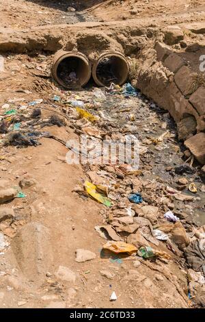 An open sewer filled with rubbish by the side of a dirt alley, Korogocho slum, Kenya, East Africa Stock Photo