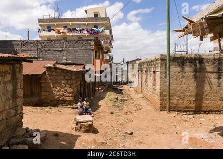 View down a dirt side alley with buildings, children and people in it, Korogocho slum, Kenya, East Africa Stock Photo