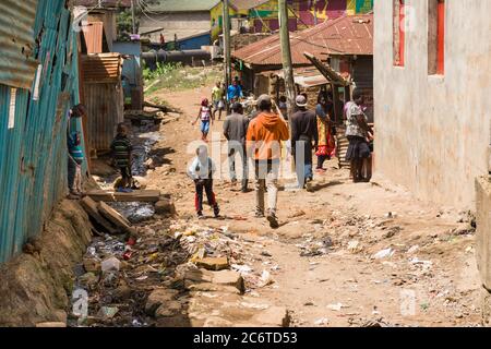 An open sewer filled with rubbish by the side of a dirt alley with residents nearby, Korogocho slum, Kenya, East Africa Stock Photo