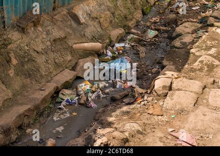 An open sewer filled with rubbish by the side of a dirt alley, Korogocho slum, Kenya, East Africa Stock Photo