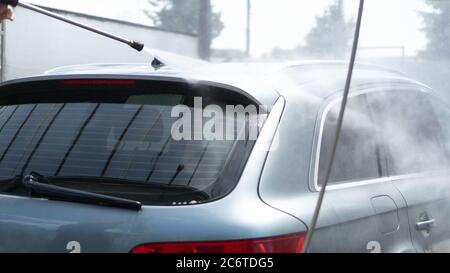 Self-service car wash. Washing a car in a carwash using a high-pressure sprayer. Gray car. Saving concept Stock Photo