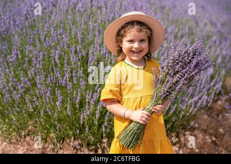 A baby girl enjoying the view and hold a bouquet of flower on her hends on a rural flower field with lavender blossoms Stock Photo