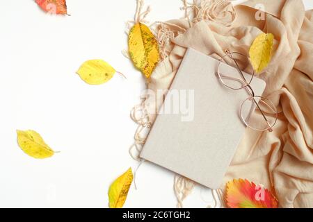 Autumn creative composition. Fallen leaves, paper notebook, women fashion glasses and beige scarf on white background. Autumn, fall concept. Flat lay, Stock Photo