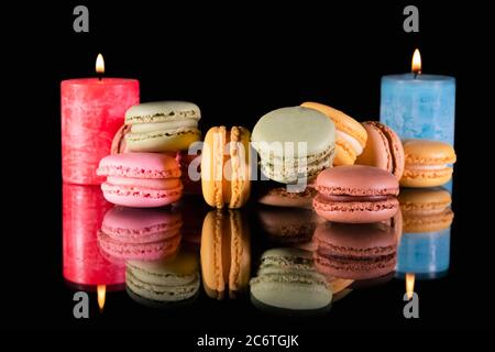 Close up of an assortment of sweet macaroons with two lit candles in the back on a reflective surface on a dark background. Stock Photo