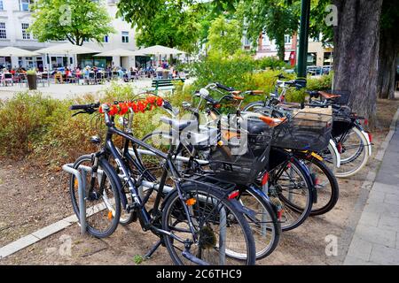 A row of parked bicycles in front of a market square with outdoor restaurant in Oberkassel near Rhine river. Stock Photo