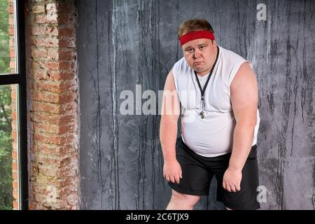 dolorous fat caucasian man with whistle in mouth, man tired doing sport exercises. isolated gray background Stock Photo