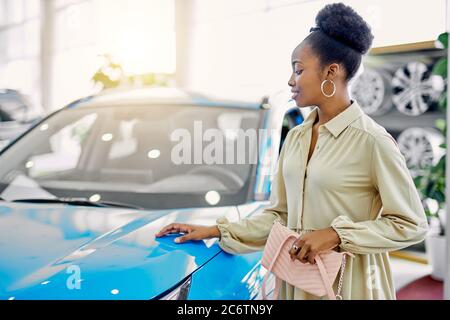 attractive afro woman dreams about new car, young female came to see automobiles, make purchase. Stock Photo
