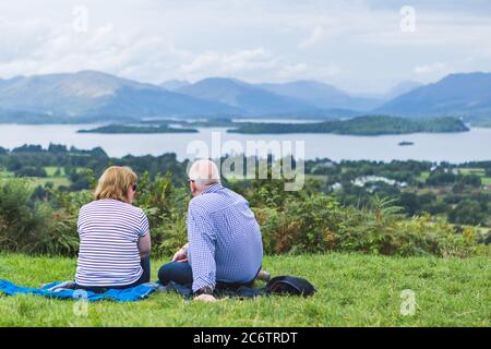 [The Trossachs, Scotland - July 2020] Enderly couple enjoy beautiful panoramic view of Trossachs landscape, Scotland Stock Photo