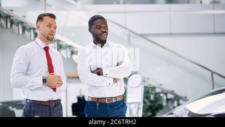 dark-skinned afro clients and confident caucasian manager or consultant are talking in car showroom, client going to buy new representative business c Stock Photo