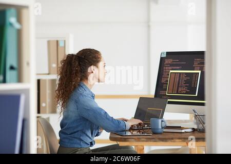 Side view portrait of female IT developer using computer while coding in modern white office interior, copy space Stock Photo