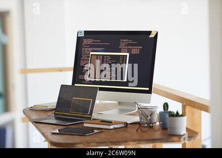 Background image of black and orange programming code on computer screen and digital devices in modern white office interior, copy space Stock Photo
