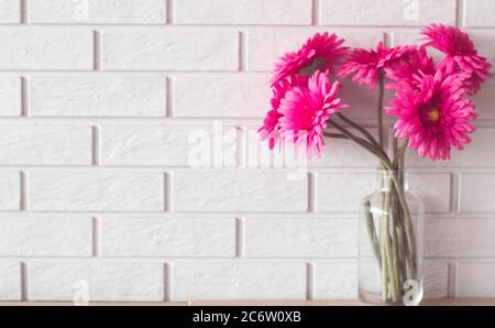 Pink Gerbera Daisies in Glass Vase on white brick wall texture background with copy space. Stock Photo