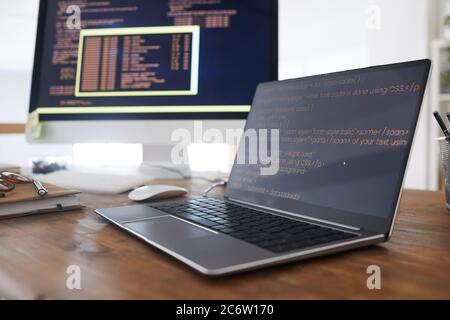 Close up background image of black and orange programming code on computer screen and laptop in contemporary office interior, copy space Stock Photo