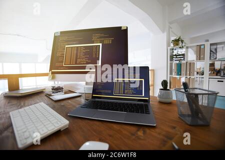 Fisheye background image of black and orange programming code on computer screen and laptop in contemporary office interior, copy space Stock Photo