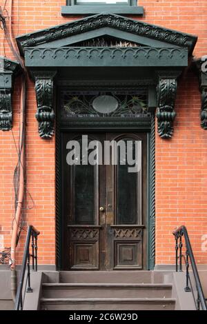 Dark brown wooden vintage entry door decorated with heavy triangular fronton, floral corbels and stained glass window. New York. USA. Stock Photo