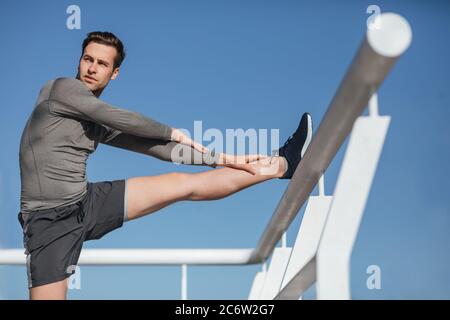 Millennial guy in sportswear doing stretching, on blue sky background Stock Photo