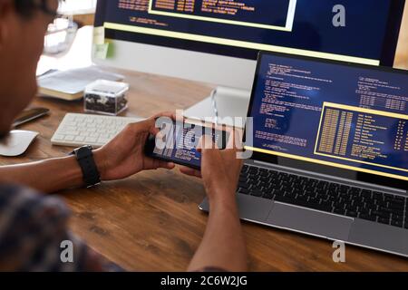 Close up of male hands holding smartphone with code on screen while working at desk in office, IT developer concept, copy space Stock Photo