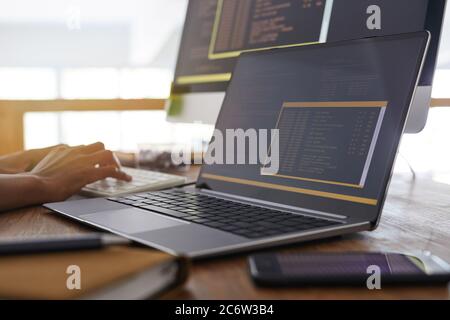Background image of male hands typing on keyboard with black and orange programming code on laptop screen in foreground, IT developer concept, copy sp Stock Photo