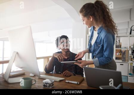 Portrait of female IT developer talking to smiling African-American colleague while standing by computers in modern office, copy space Stock Photo