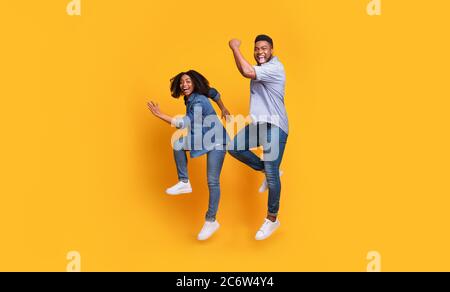 Funny African Couple Jumping In The Air And Laughing Over Yellow Background Stock Photo