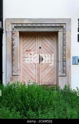 Wooden vintage entry door decorated with floral plaster molding with green bushes in the foreground. Wroclaw. Poland. Stock Photo
