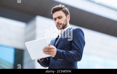 Corporate employee in formal suit checking mail on tablet computer at city street Stock Photo