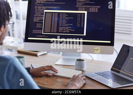 Back view portrait of African-American man writing code on computer screen while working at desk in IT development studio, copy space Stock Photo