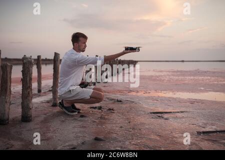 A young man launches a drone from his hand on a pink salt lake in Ukraine. Stock Photo