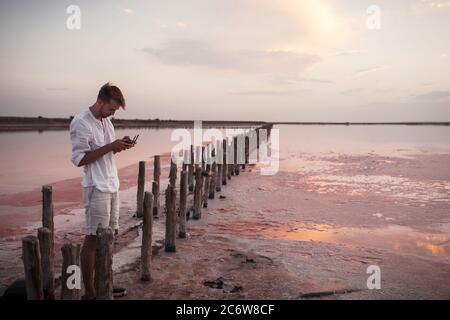 A young man controls a drone from a remote control panel on a pink salt lake in Ukraine. Stock Photo