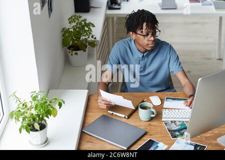 High angle portrait of creative African-American man reviewing photographs while working on editing and publishing in modern office, copy space Stock Photo