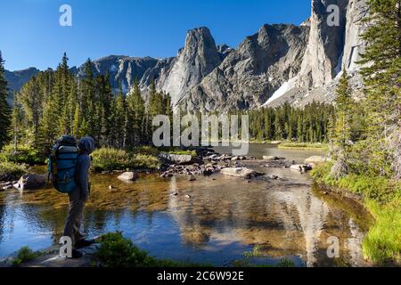 A male backpacker travelling on the North Fork Trail pauses along the North Popo Agie River to take in the view of a lake and cirque. Stock Photo