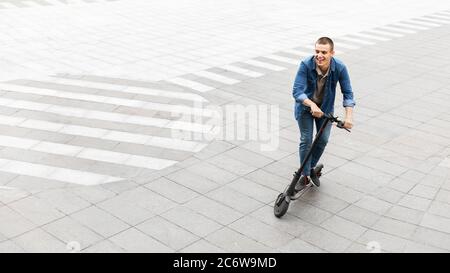 Happy guy having pleasant ride on electric kick scooter Stock Photo