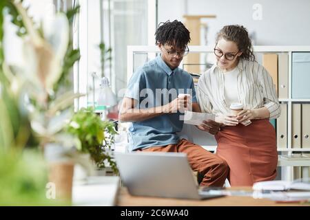 Portrait of two creative young people looking at printed photographs during coffee break in modern office, copy space Stock Photo
