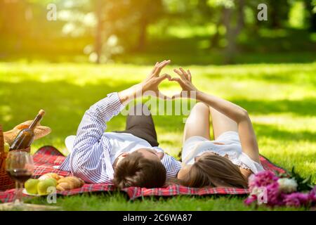 Affectionate young couple making heart with their hands while lying on picnic blanket at park Stock Photo