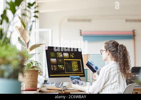 Portrait of young female photographer using computer at desk in home studio with photo editing software on screen, copy space Stock Photo