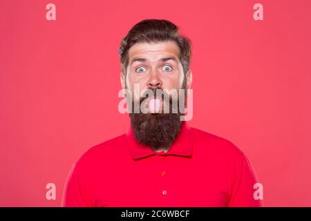 Pink tongue. Bearded and cheerful. Hipster appearance. Beard fashion. Barber concept. Man bearded hipster red background. Barber tips. Barbershop model. Cute face. Having fun. Showing long tongue. Stock Photo