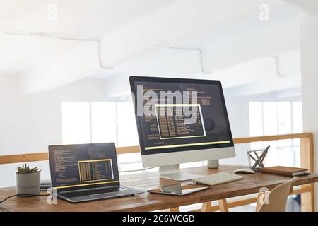Background image of two computers with programming code on screen in minimal home office interior with wooden accents, copy space Stock Photo