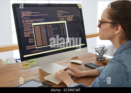 Portrait of young woman writing programming code on computer screen while working at desk in contemporary office interior, copy space Stock Photo