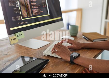 Close up of African-American computer programmer typing on keyboard with black and orange programming code on computer screen, copy space Stock Photo