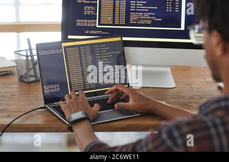 Back view at African-American IT developer typing on keyboard with black and orange programming code on computer screen and laptop, copy space Stock Photo