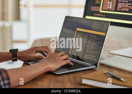 Close up of African-American computer programmer typing on keyboard with black and orange programming code on laptop screen, copy space Stock Photo