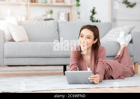 Pensive young woman using digital tablet at home, relaxing on floor Stock Photo